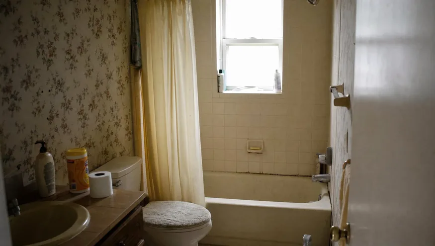 Outdated 1990s bathroom with a worn standard bathtub before renovation